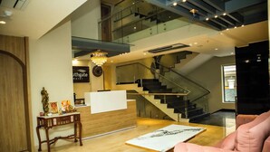 A hotel reception area with a wooden desk, a reception counter, and a staircase leading to an upper floor. - Hotel Southgate Goa (Calangute)