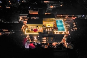 Vista aérea de un hotel moderno con piscina, varios balcones y zonas exteriores bien iluminadas.