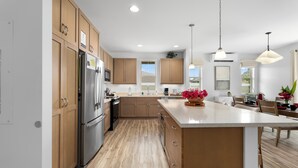 A modern kitchen with wooden cabinets, stainless steel appliances, and a central island with a vase of flowers. - Pakele Oahu by AvantStay | 5 Min to Makaha Beach (Waianae)