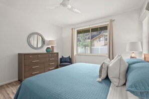 Een slaapkamer met een bed, dressoir, raam en plafondventilator.