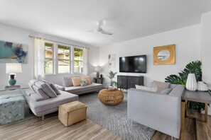 Een moderne woonkamer met een bank, een poef en een aan de muur bevestigde televisie.
