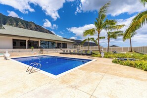 Une piscine à l’eau d’un bleu cristallin, entourée d’une terrasse en béton, de palmiers et d’un bâtiment doté de grandes fenêtres.