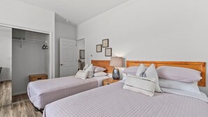 A hotel room with two beds, a wardrobe, a bedside table with a lamp, and a door leading to a bathroom. - Pakele Oahu by AvantStay | 5 Min to Makaha Beach (Waianae)
