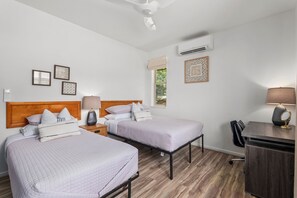 Une chambre d’hôtel avec deux lits, un bureau, une chaise et une fenêtre donnant sur un paysage verdoyant.