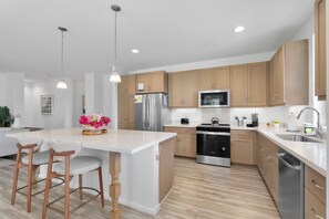Une cuisine moderne avec des meubles en bois, des appareils électroménagers en acier inoxydable et un îlot central doté de tabourets de bar.