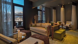 Un salon moderne comprenant un canapé, des poufs, une table basse et offrant une vue sur un paysage montagneux grâce à de grandes fenêtres.