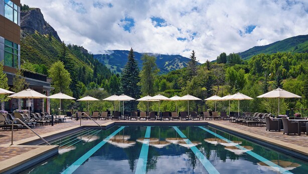 Un espace piscine doté de chaises longues et de parasols, entouré de montagnes et de verdure.