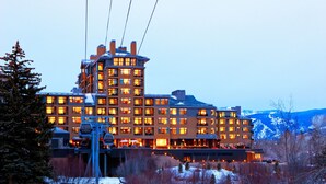 Un grand hôtel à plusieurs étages, avec un télésiège et, en arrière-plan, des montagnes enneigées.