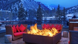 Un foyer extérieur agrémenté de coussins rouges, situé sur un balcon donnant sur un paysage montagneux enneigé.