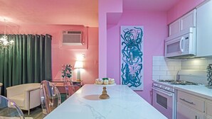 A kitchen with a marble countertop, a gas stove, white cabinets, and a pink wall.