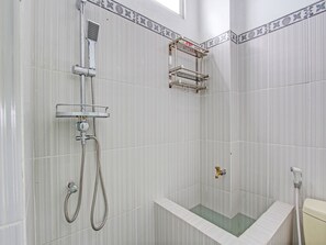 A bathroom with a shower, toilet, and a small shelf unit. - Hotel O Wisma Ratu Syariah (Sukoharjo)