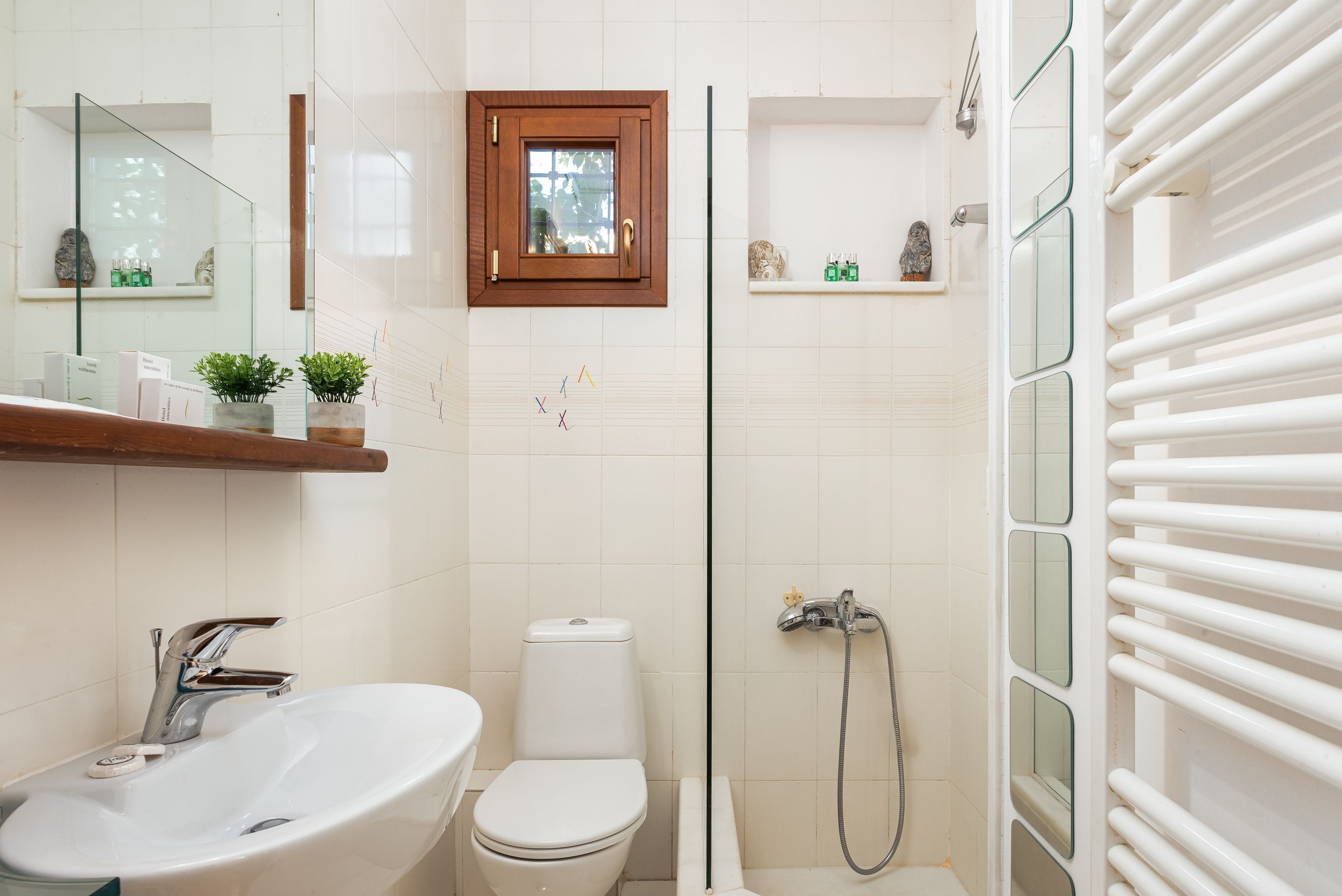 A bathroom with a white sink, toilet, and shower. There is a wooden medicine cabinet above the sink and a small shelf with toiletries.