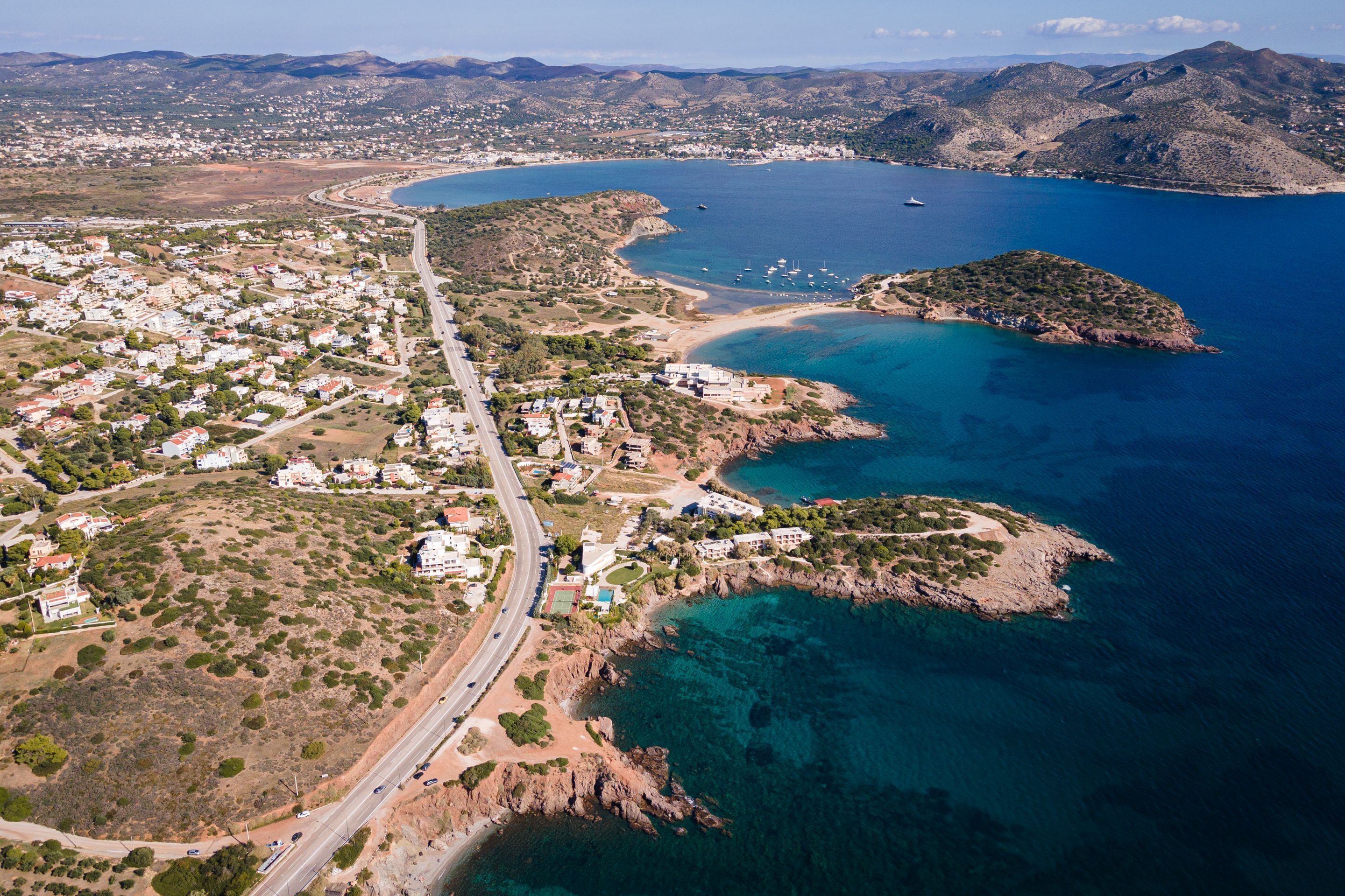 Vista aérea de uma cidade costeira, com uma estrada principal, áreas residenciais e águas azul-claras.