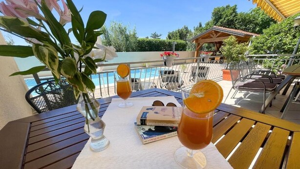 A table with drinks, books, and a view of a pool and greenery. - Apartment in Croatia near Adriatic Coast (Jadranovo)