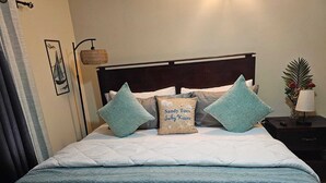 Un lit bien fait, avec une couette blanche matelassée, deux coussins turquoise et un coussin décoratif orné d’un motif textuel.