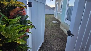 Un étroit sentier mène à un bâtiment entouré d’une clôture blanche et doté d’un petit jardin.