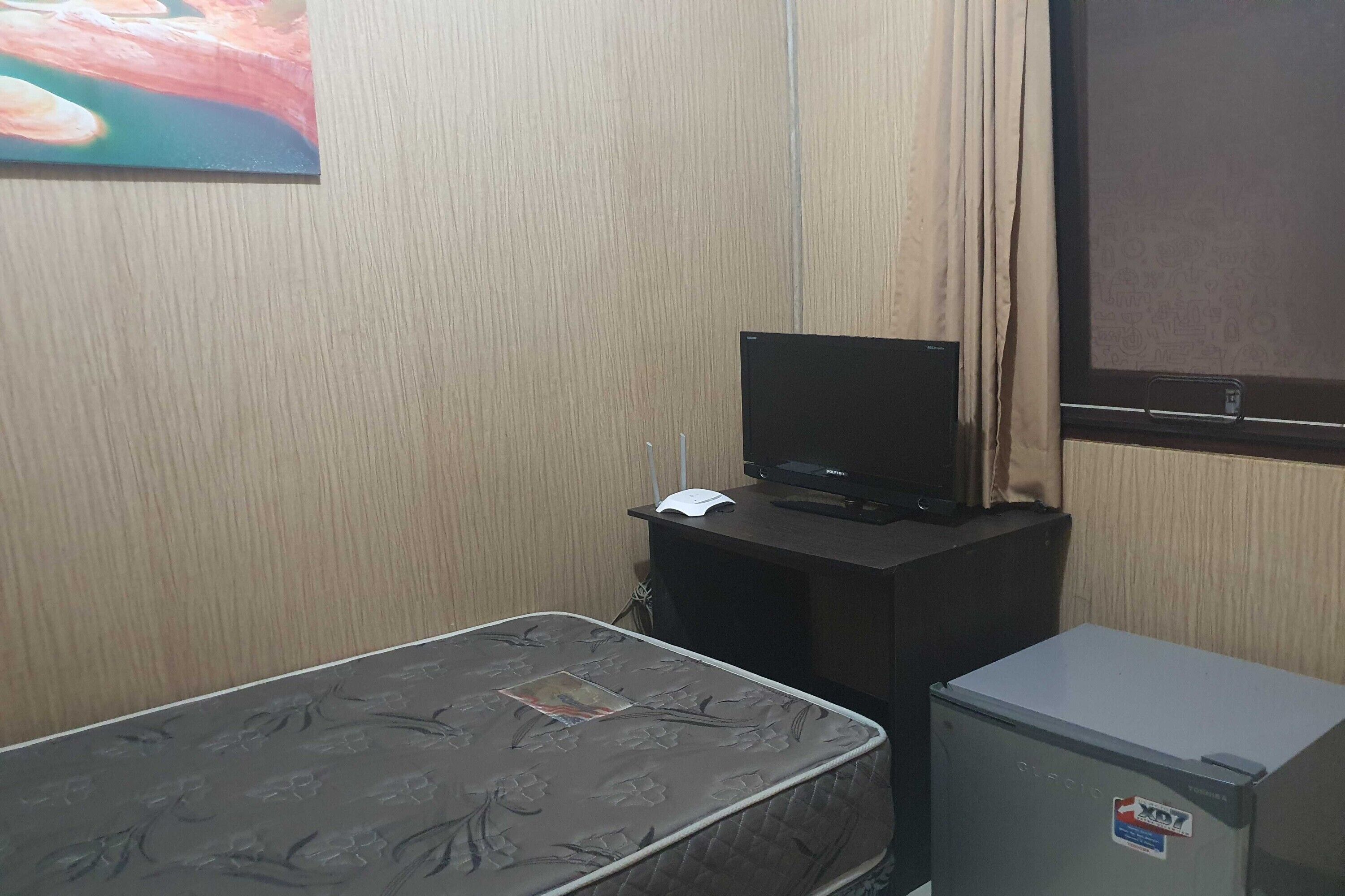 A small room with a bed, a desk with a computer, and a refrigerator.
