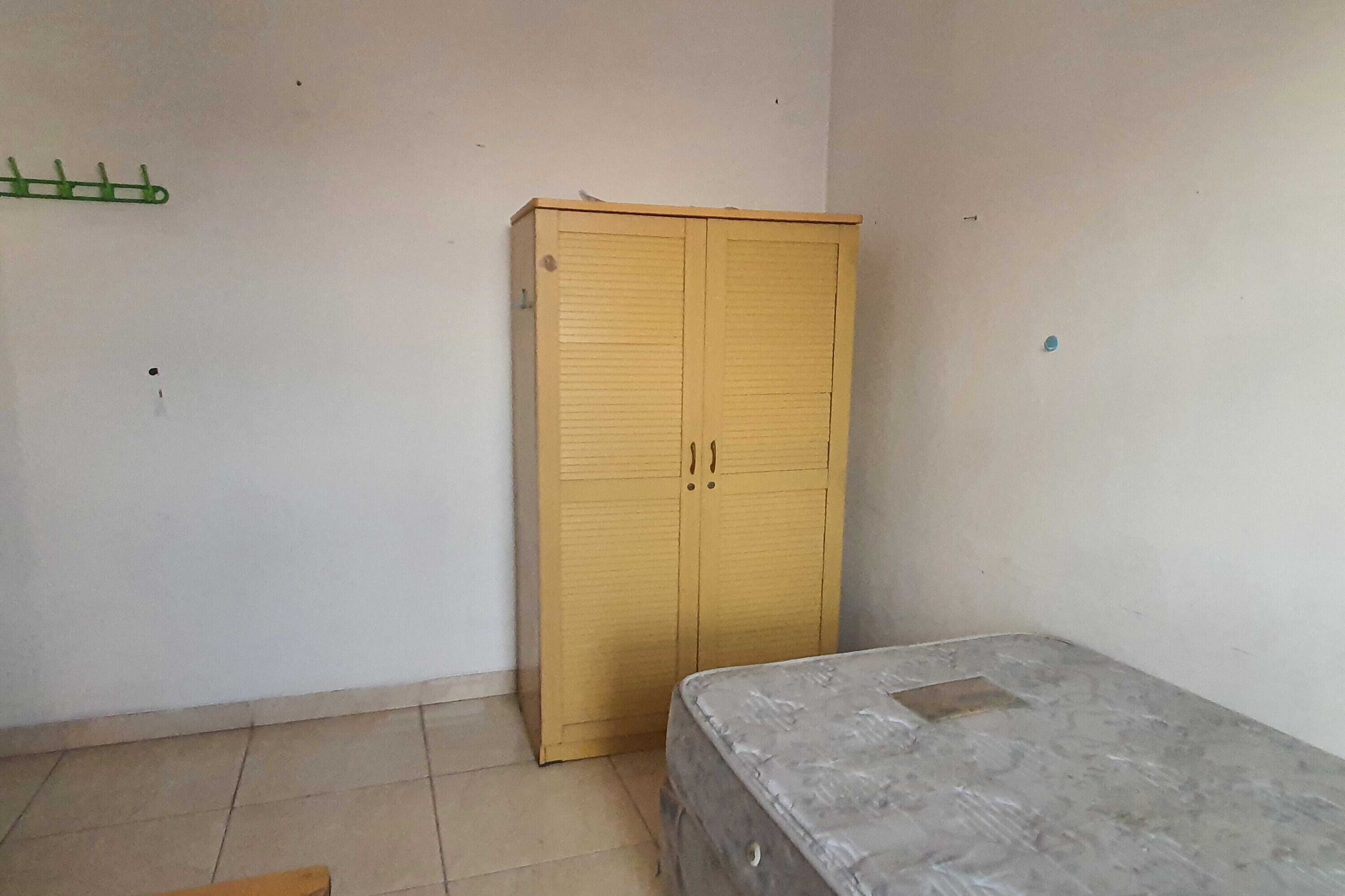 A room with a single bed, a wooden wardrobe, and a green coat rack.
