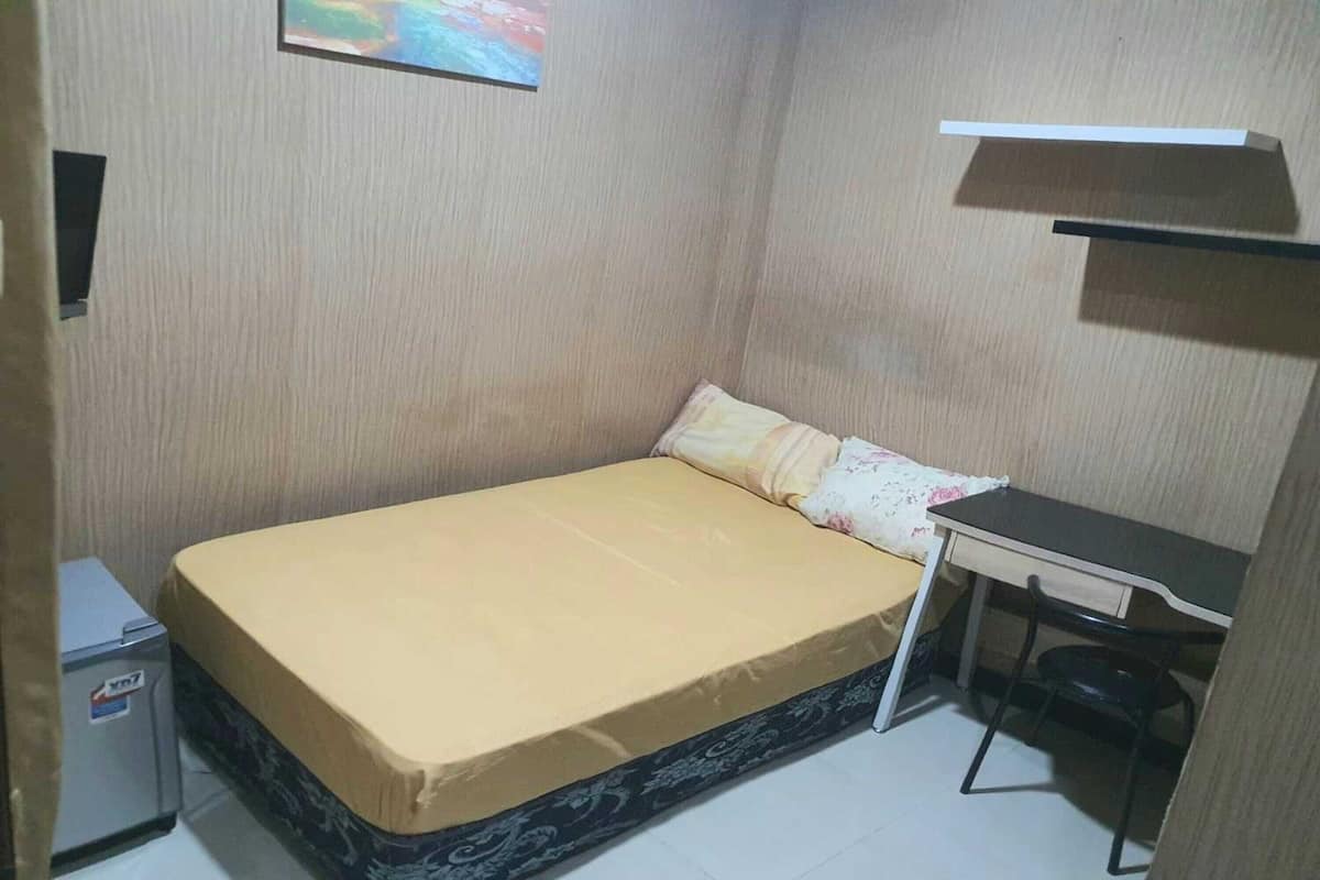 A small, compact room with a single bed, a desk, and a chair.