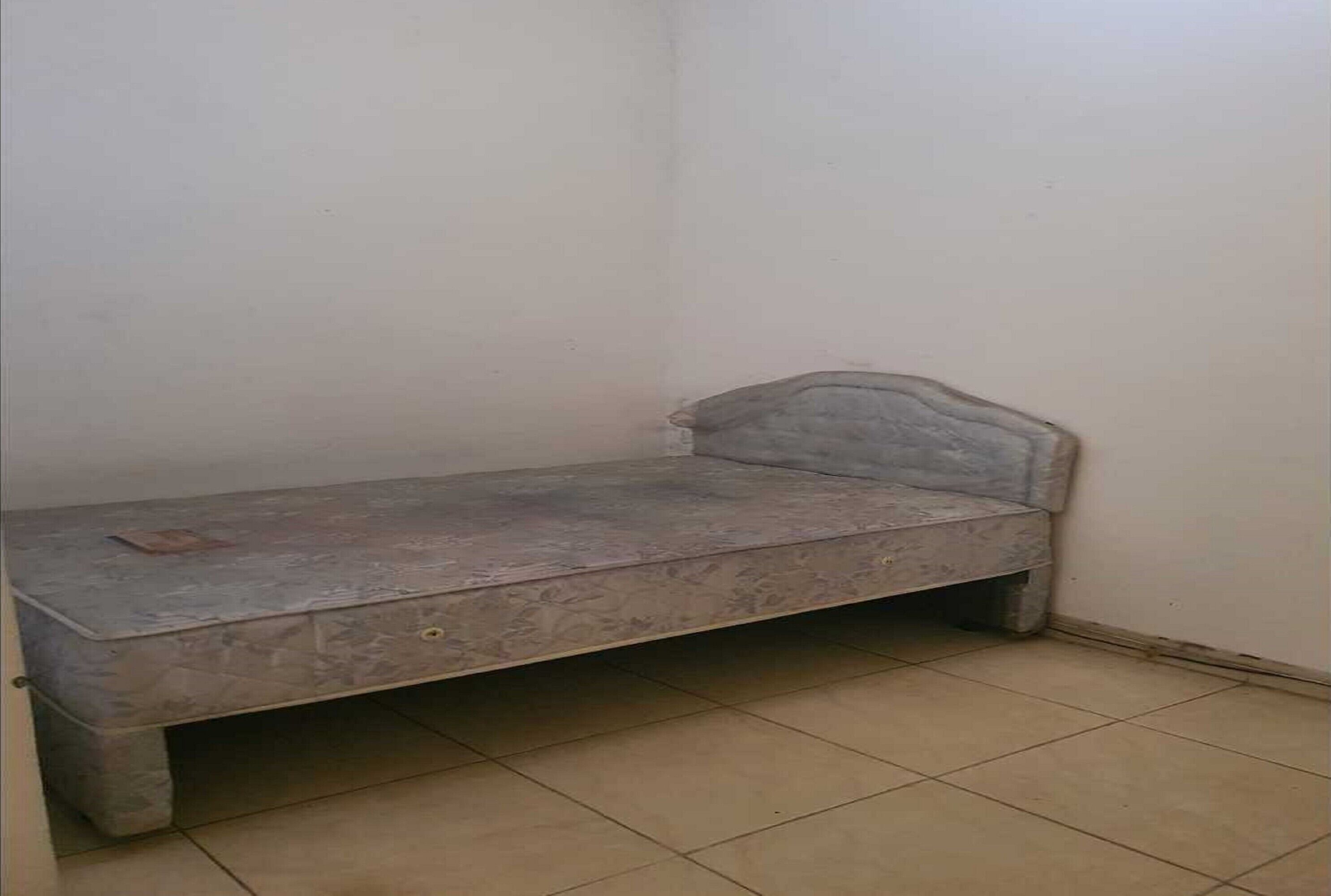 Una habitación pequeña con una cama individual, un cabecero sencillo y una mesita.