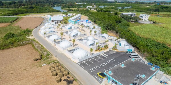 An aerial view of a facility with multiple dome-shaped structures, a parking area, and surrounding greenery.