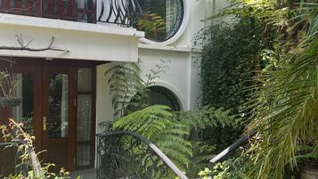 A two-story building with a balcony, large windows, and a garden area with various plants and a stone pathway.