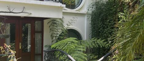 A two-story building with a balcony, large windows, and a garden area with various plants and a stone pathway.