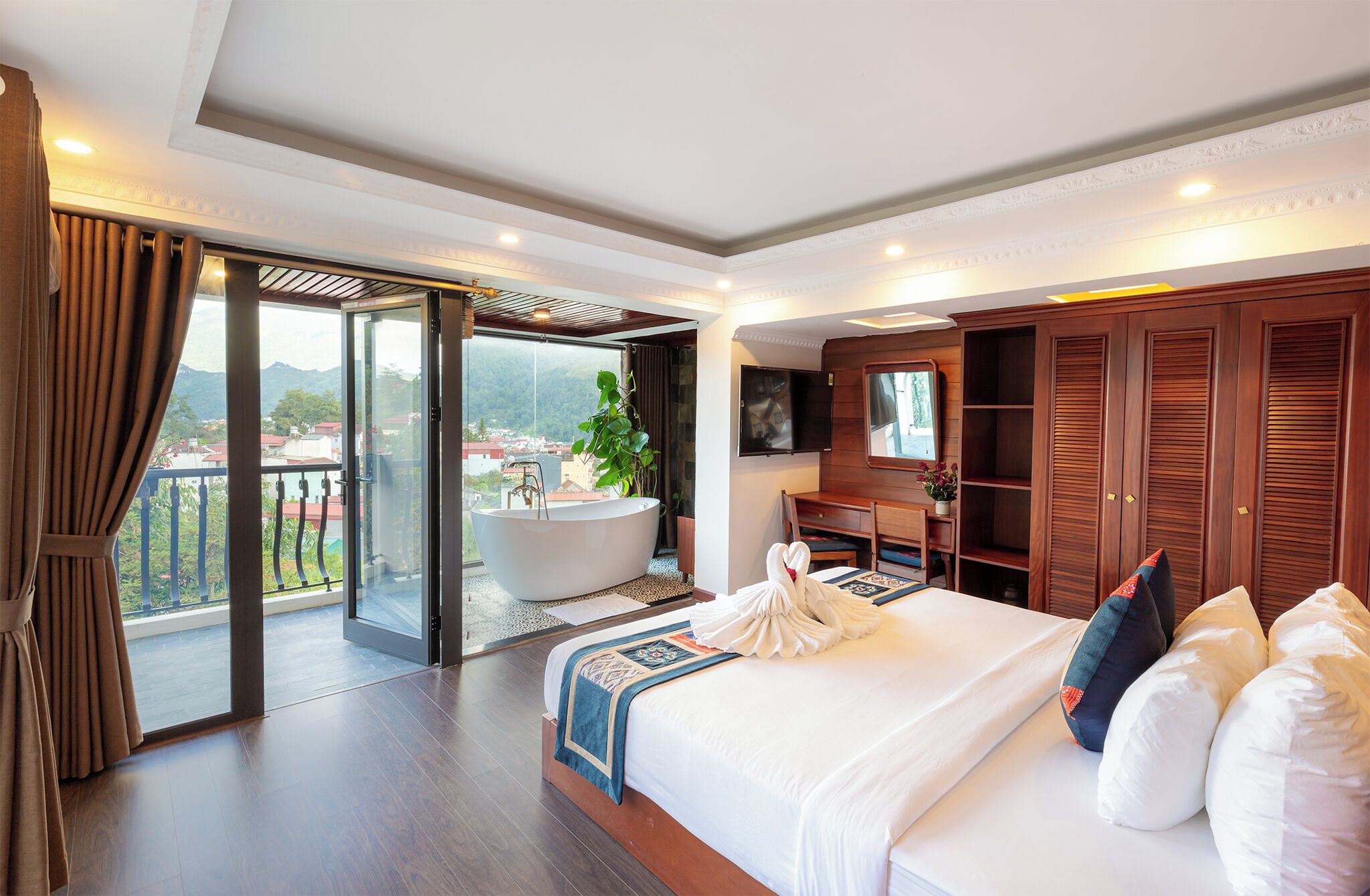 A hotel room with a large bed, a bathtub, a TV, and a sliding glass door to a balcony.