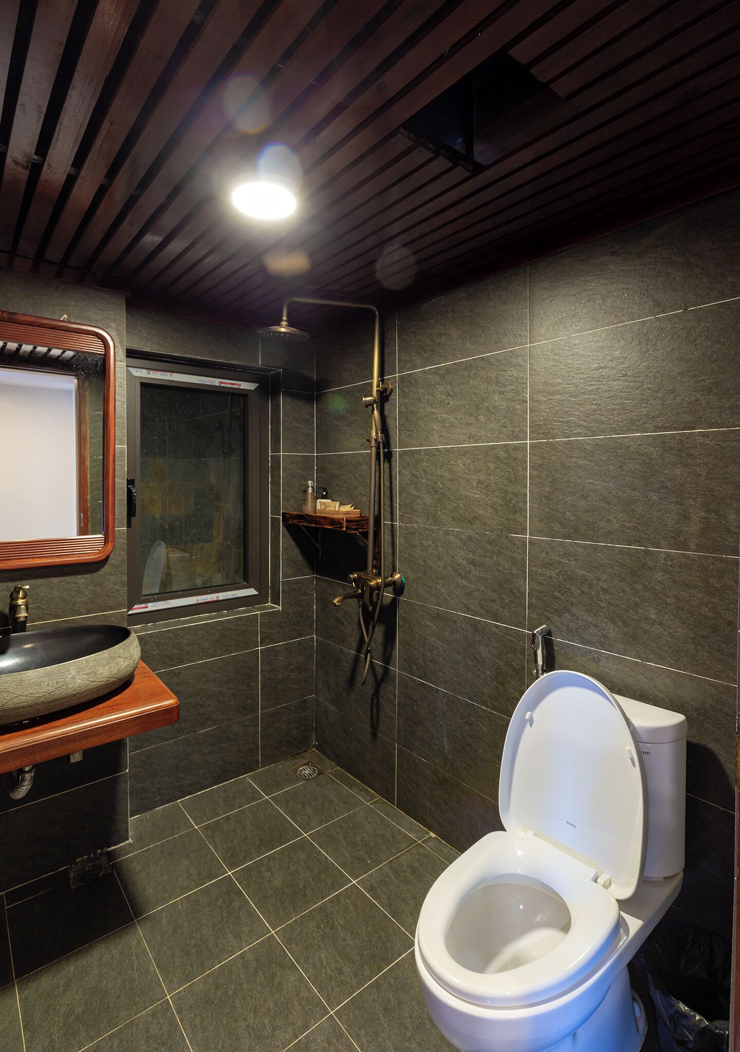 A modern bathroom with a wooden vanity, a white toilet, a shower area, and a mirror.