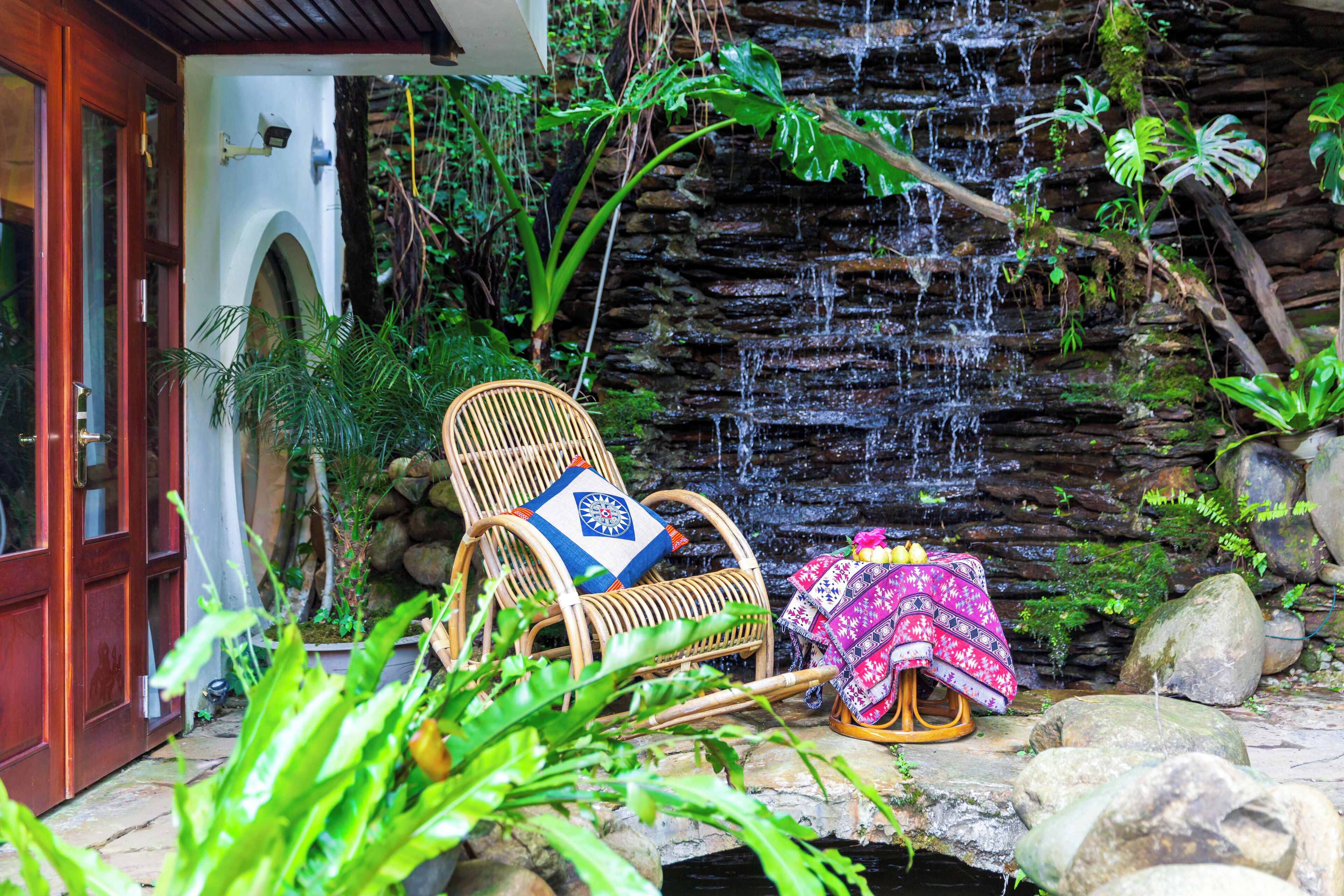 A stone waterfall, a wicker chair with a cushion, and a colorful blanket on a stone ledge.