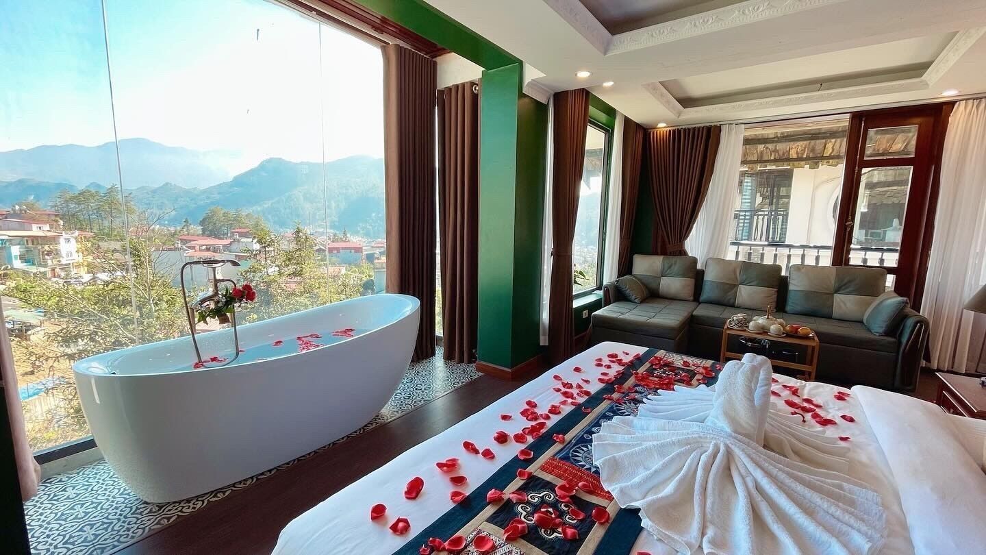 Een hotelkamer met een ruime badkuip, een bed met rozenblaadjes, een sofa en uitzicht op bergen.