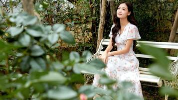 Une femme est assise sur un banc blanc, entourée de verdure.