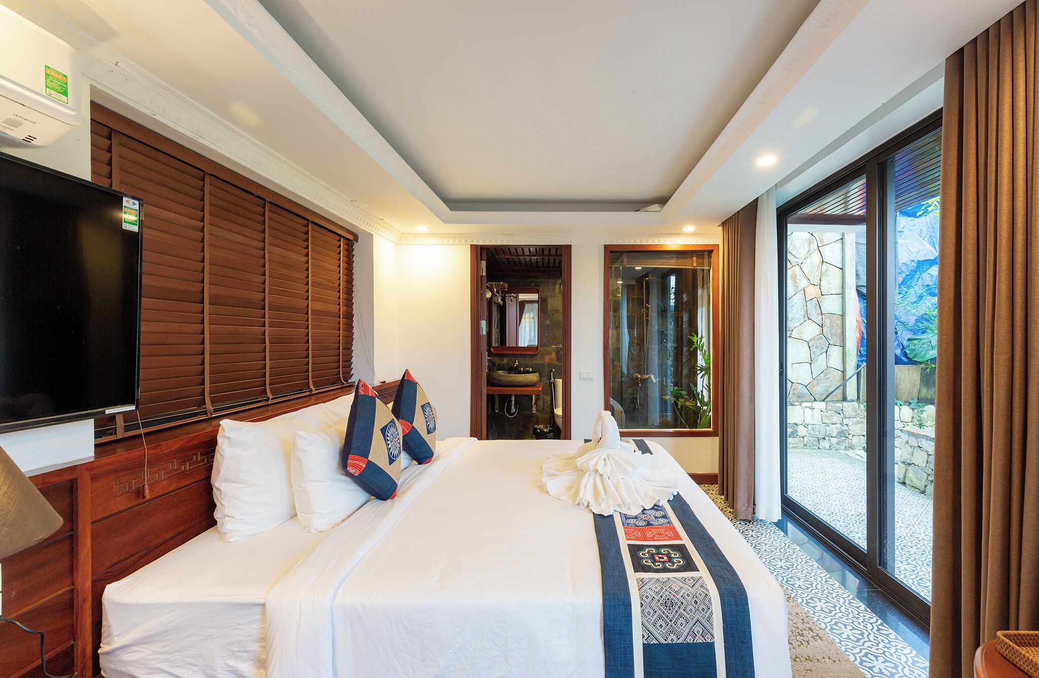 A hotel room with a large bed, a television, a bathroom with a sink and mirror, and a view of the outdoors.