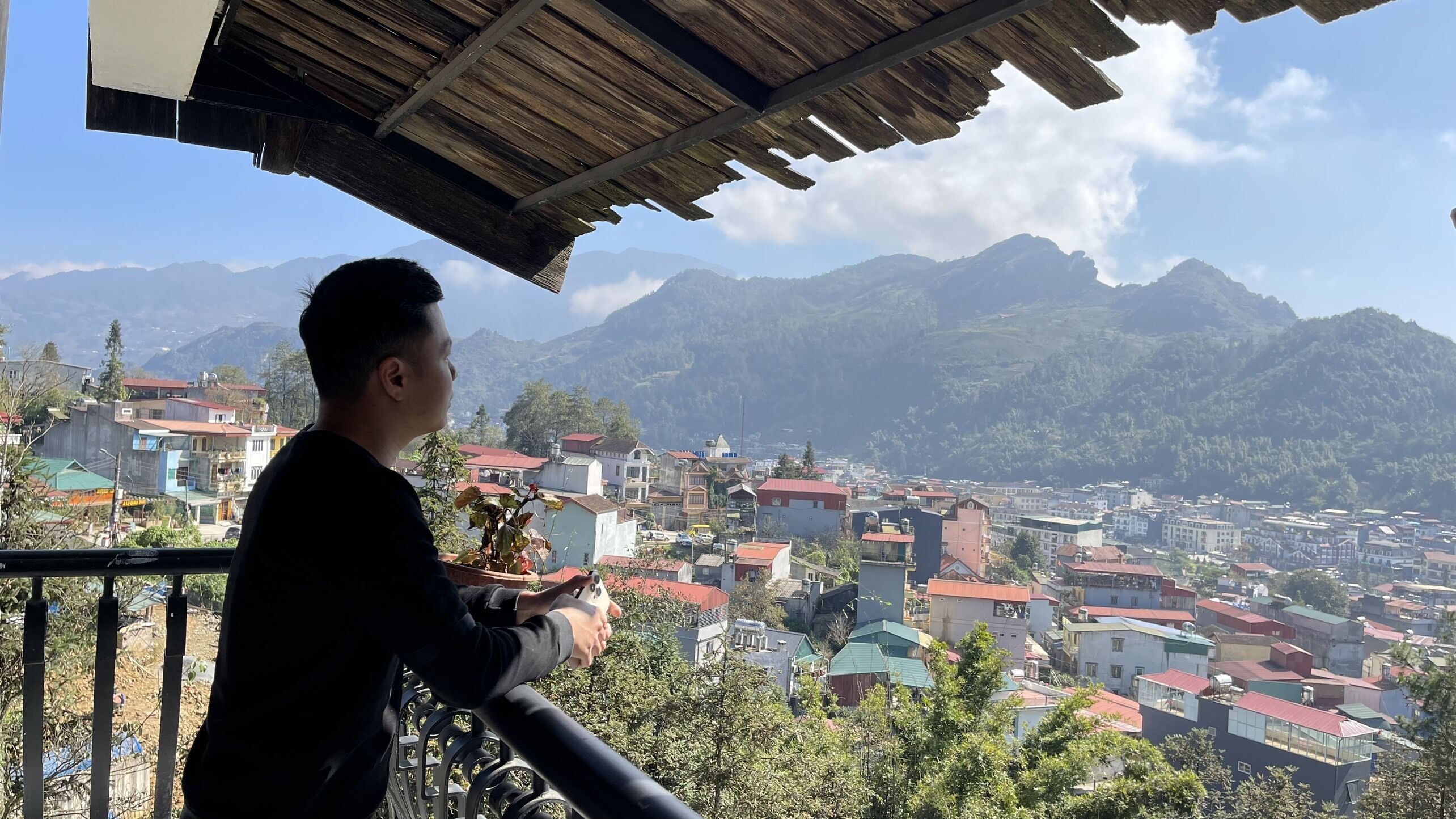 A person sitting on a balcony overlooking a town with mountains in the background.