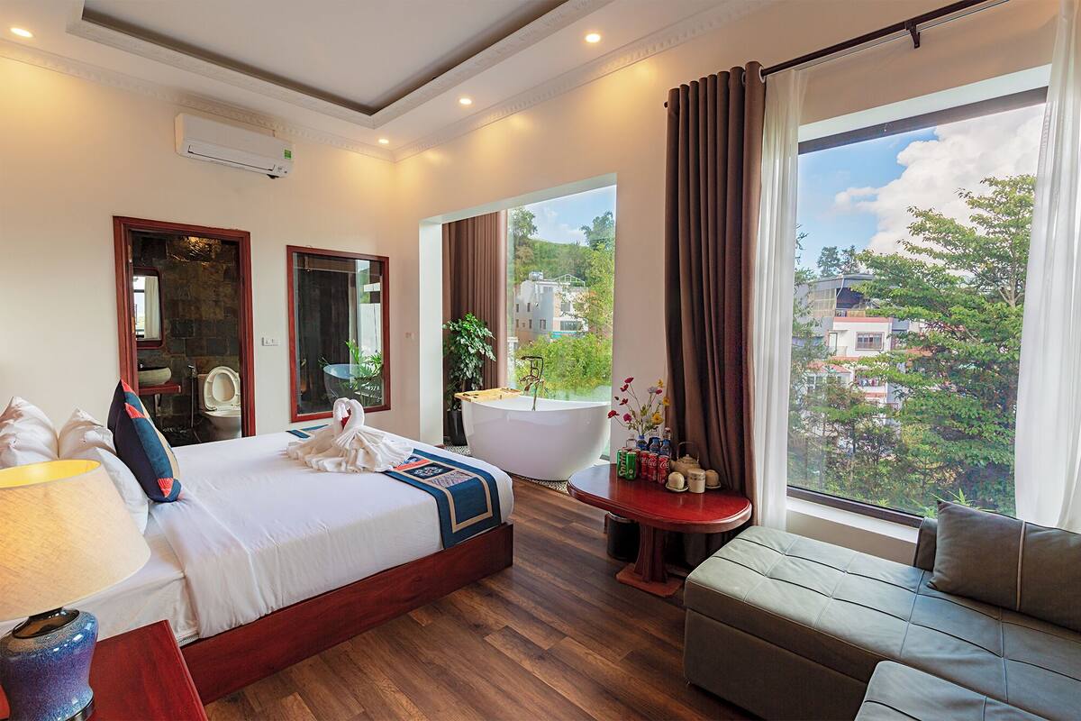 A hotel room with a bed, a bathtub, a sofa, and a large window with a city view.