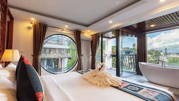 Een hotelkamer met een groot bed, een ronde spiegel, een badkuip en een balkon met uitzicht op de bergen.