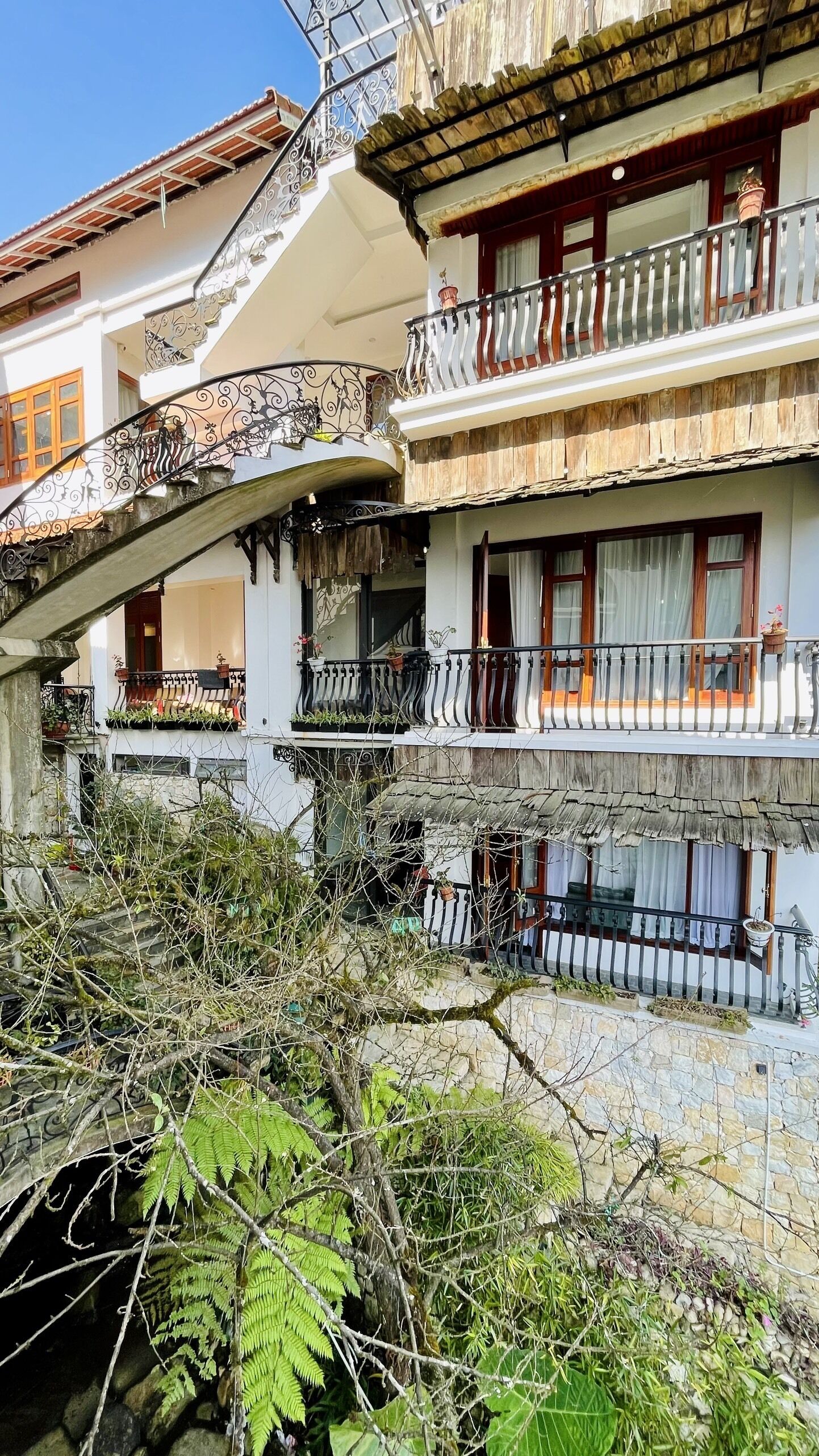 A multi-story building with balconies, stone walls, and potted plants.