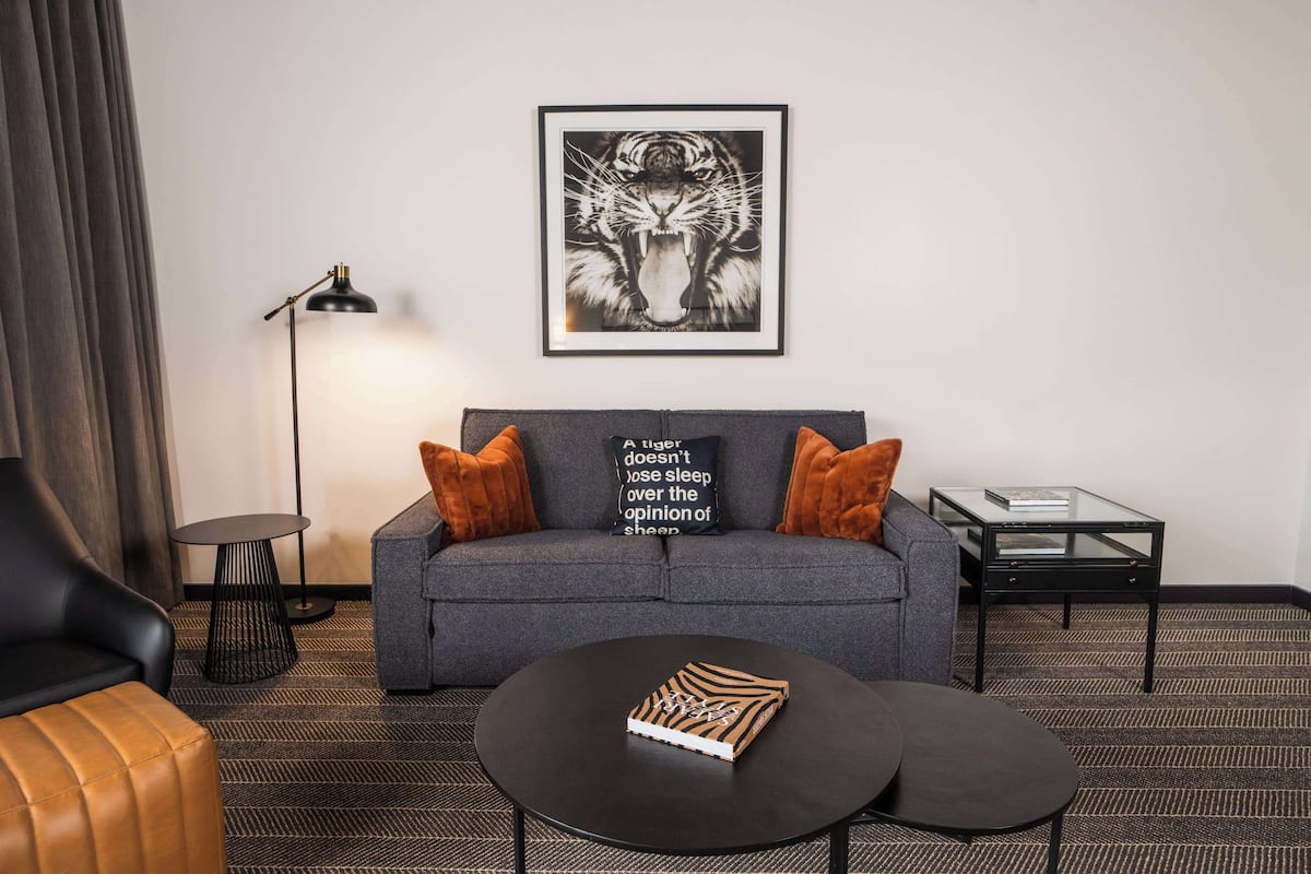 A modern hotel room with a grey sofa, black coffee table, and a framed tiger artwork on the wall.