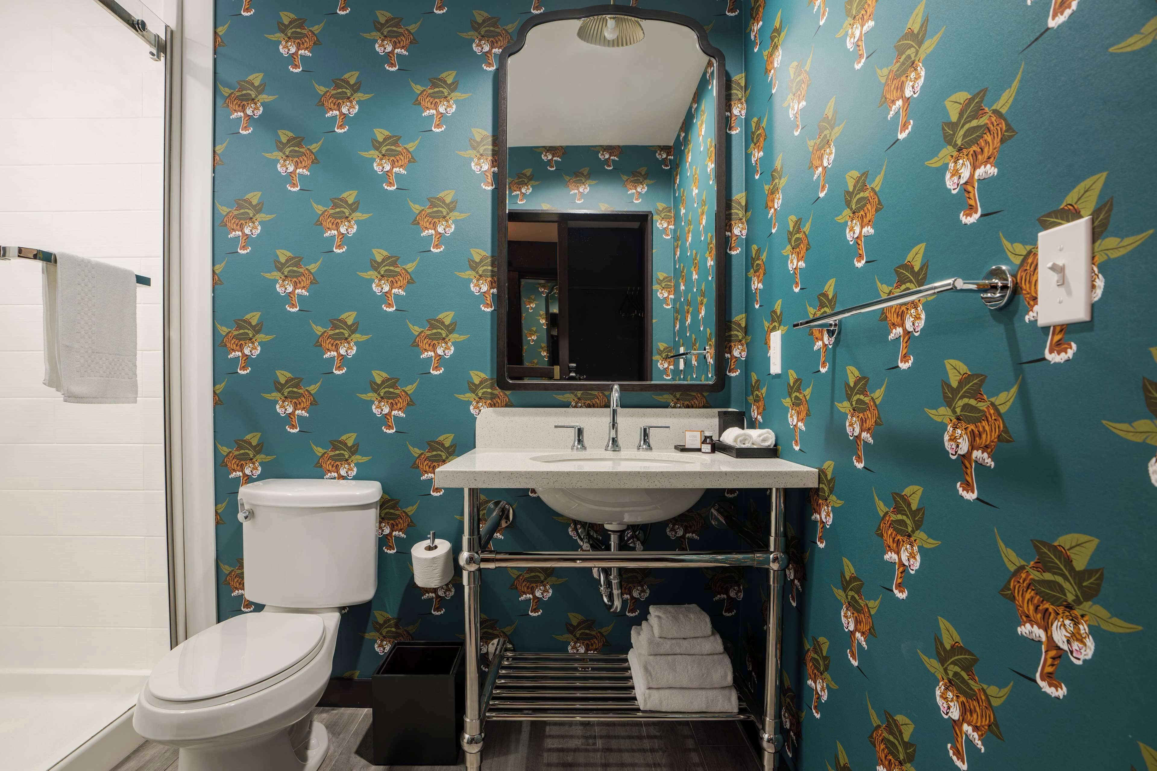 Un baño con inodoro, lavamanos y espejo. Las paredes están decoradas con un estampado de tigre.