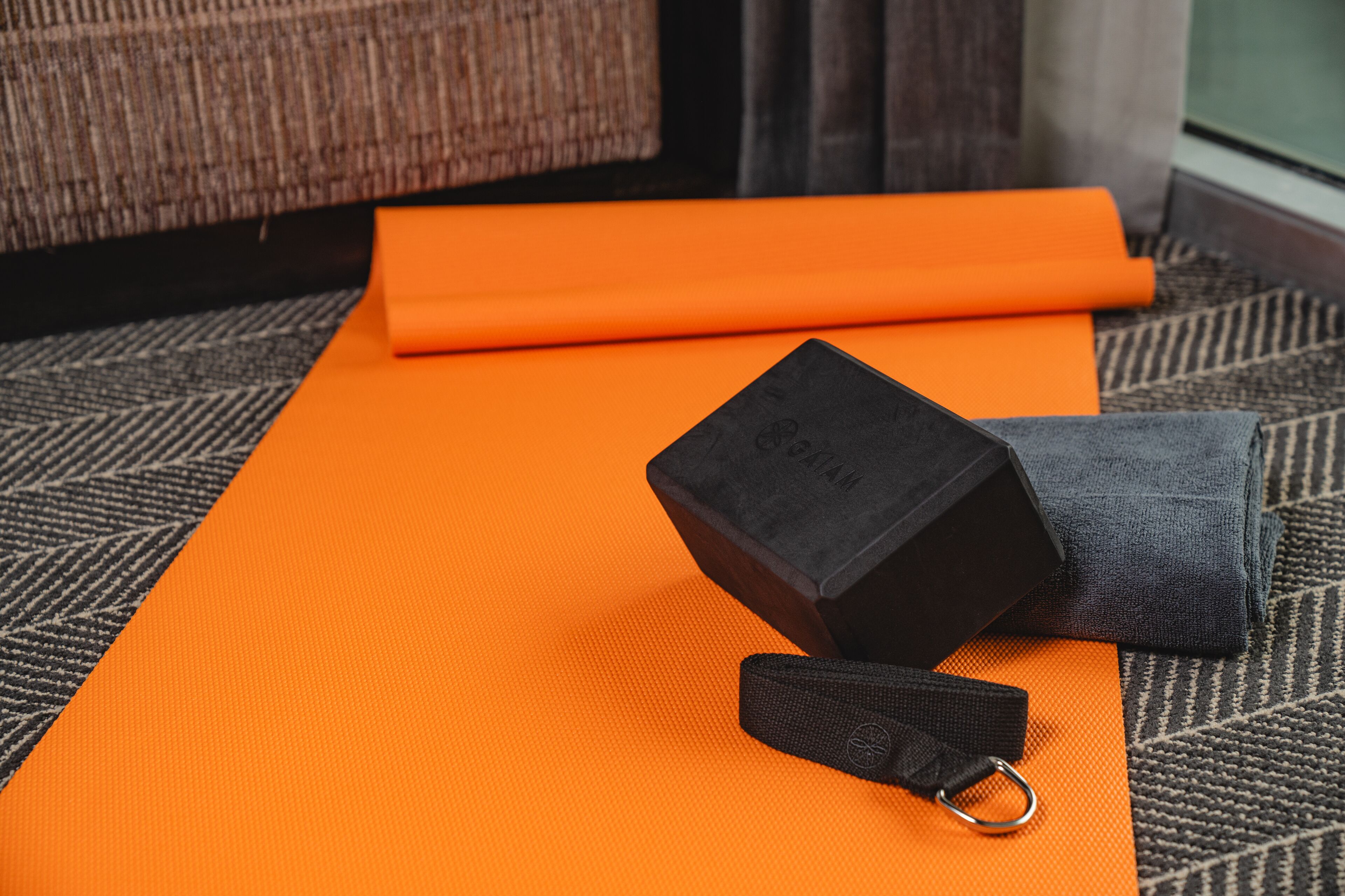 Un tapis de yoga, une paire de disques d’haltères noirs et un élastique de résistance noir, le tout posé sur un tapis orange.