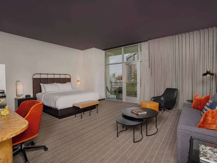 Una habitación de hotel con una cama, un sofá, una mesa de comedor y un pequeño balcón.