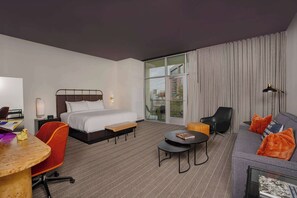 A hotel room with a bed, a sofa, a dining table, and a small balcony.