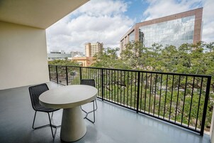 Un balcón con una mesa redonda y dos sillas, con vista a un paisaje urbano de edificios modernos y áreas verdes.