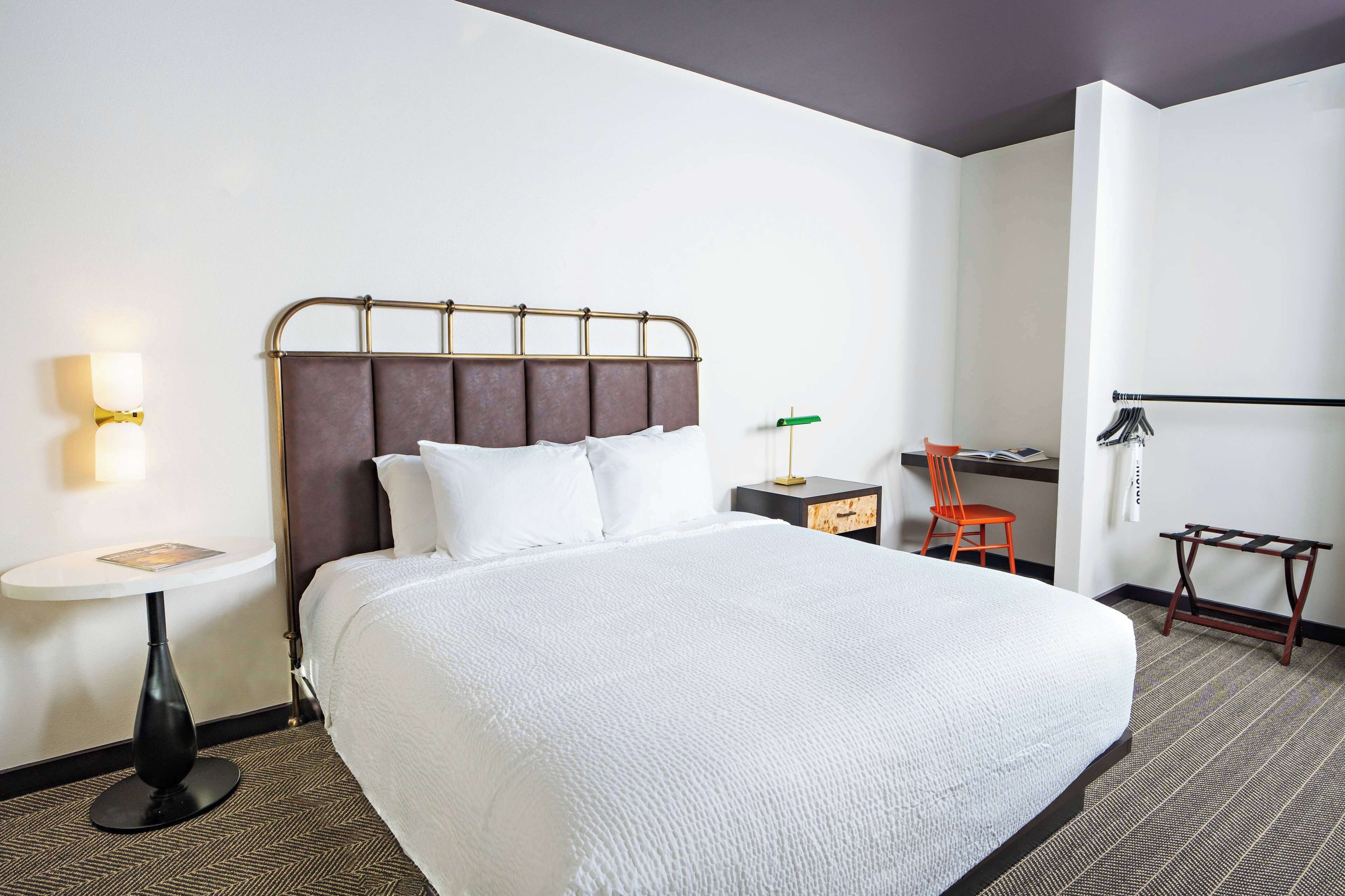 Una camera d'albergo ordinata con un letto grande, una piccola scrivania, una sedia e un comodino.
