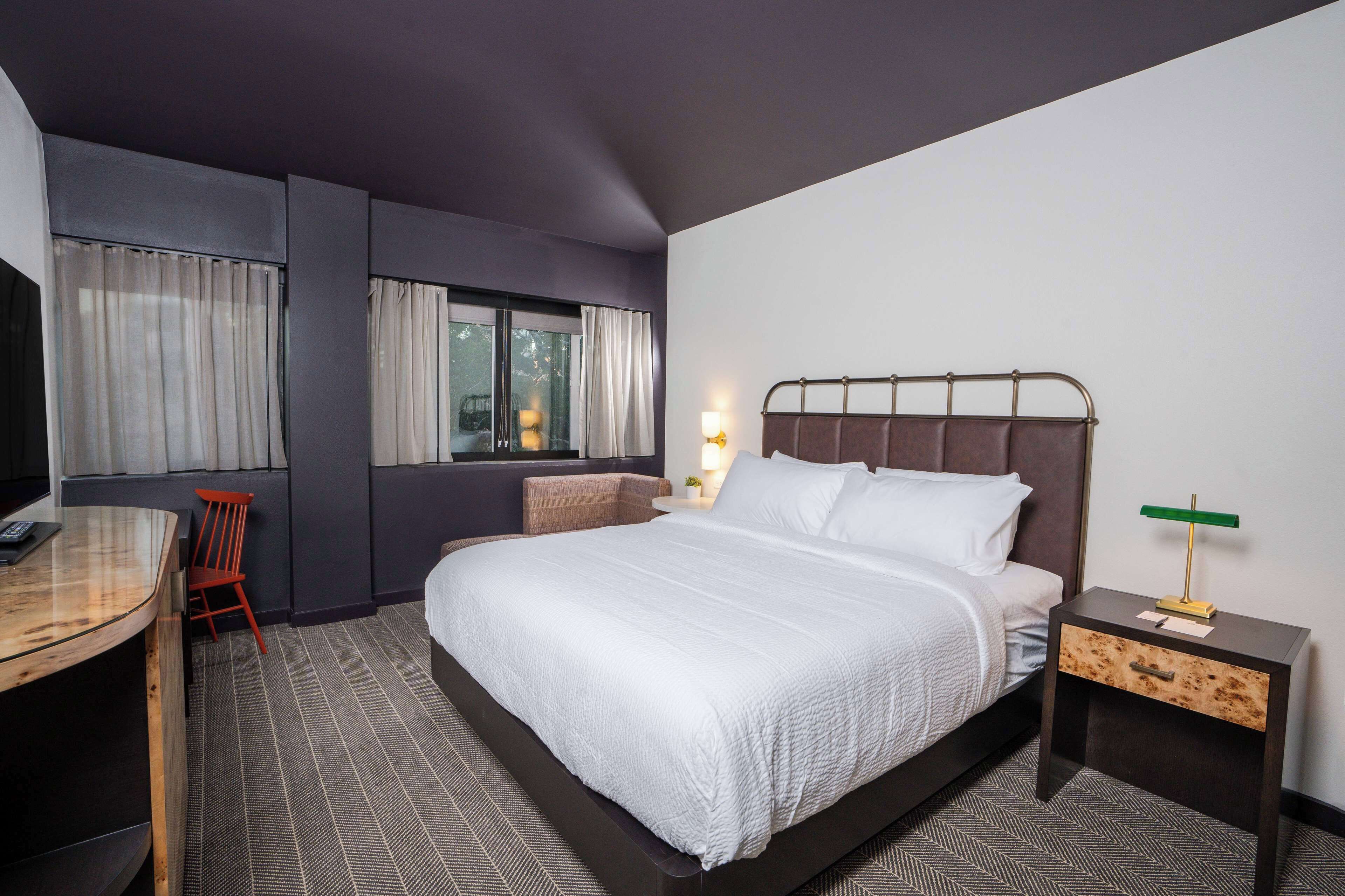 Une chambre d’hôtel avec un grand lit, un bureau, une chaise, une télévision et une fenêtre avec des rideaux.