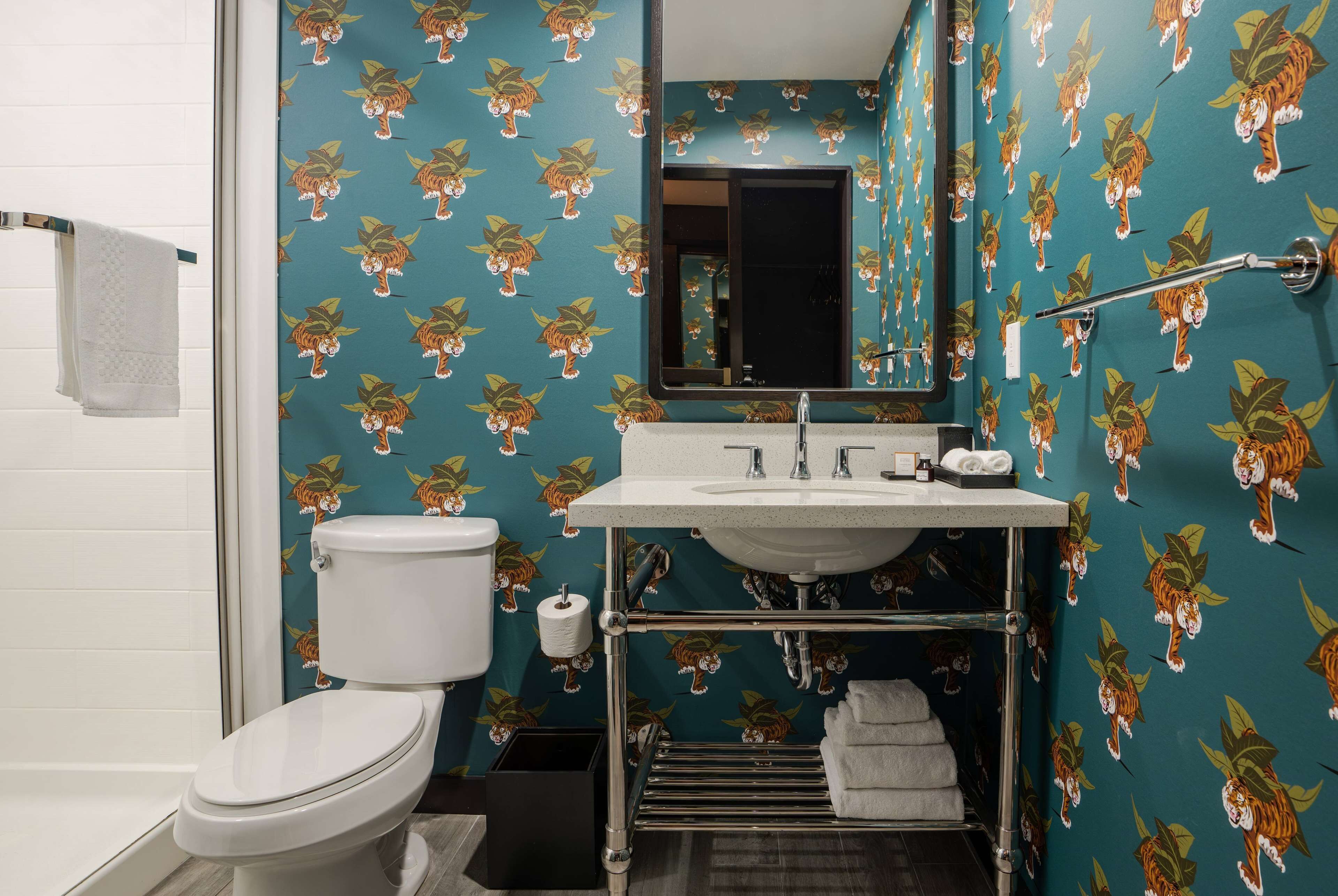 A bathroom with a toilet, sink, and mirror. The walls have a tiger print wallpaper.
