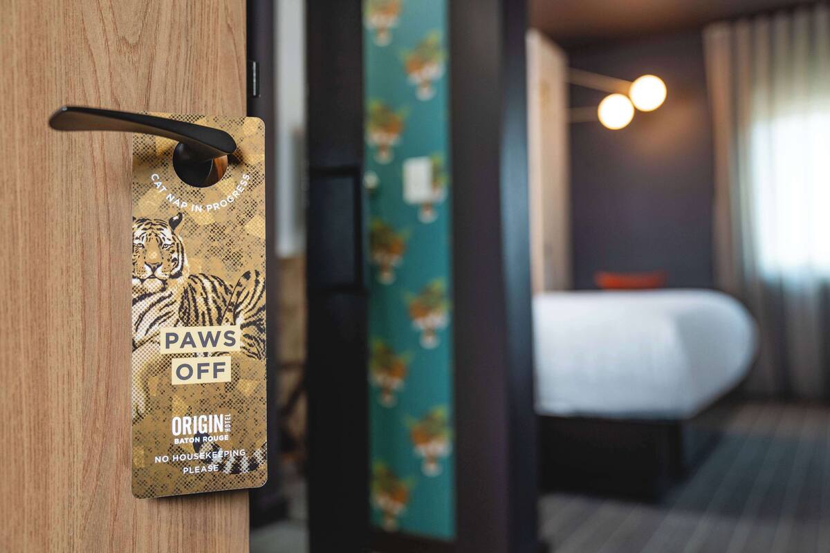 A hotel room with a wooden door, a bed, and a wall with a floral pattern.
