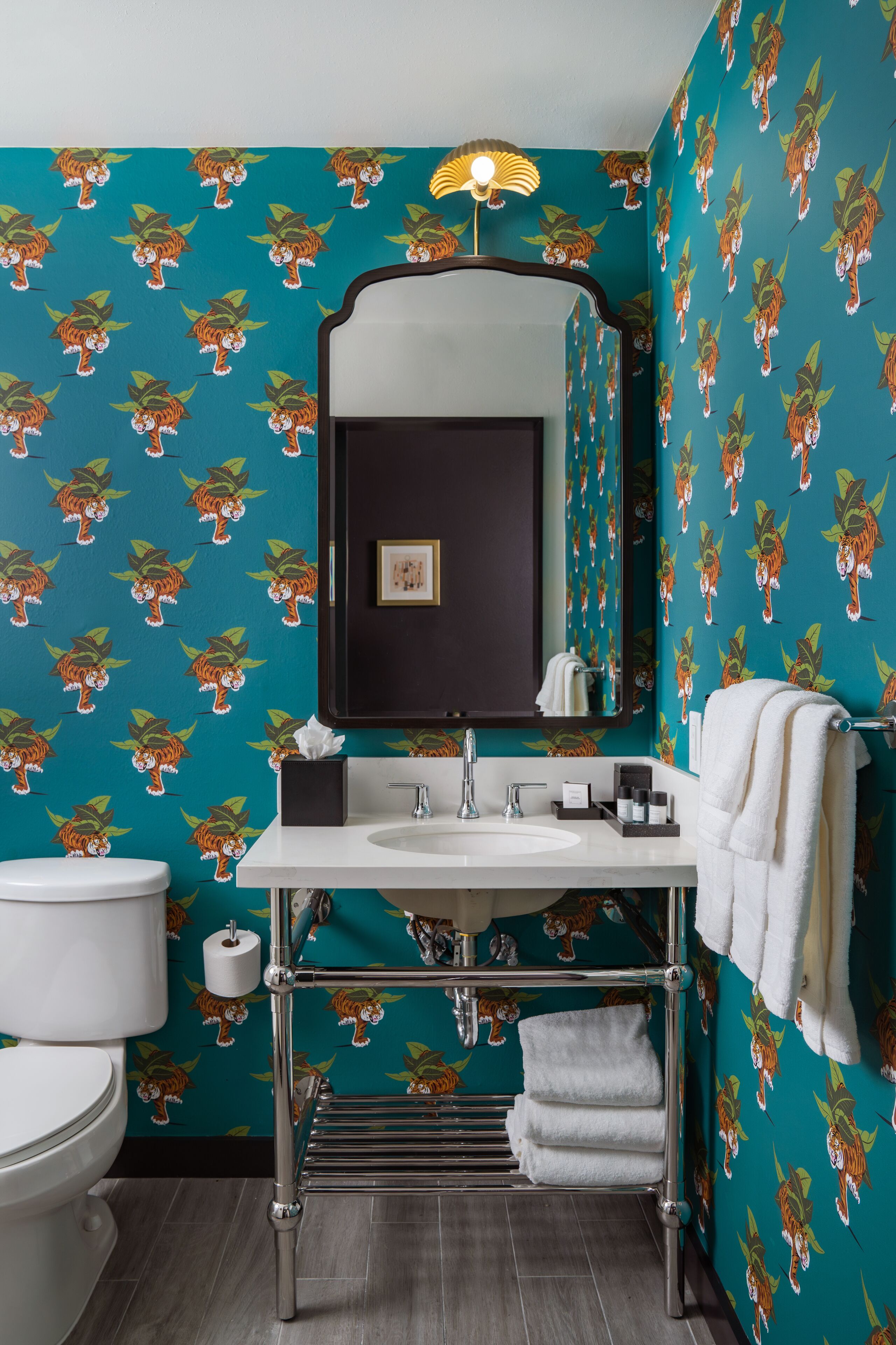 Un baño con inodoro, lavamanos, espejo, toallero y papel tapiz estampado.
