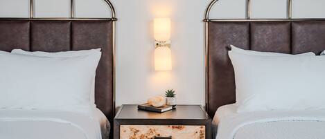 A double bed with a nightstand in between, a wall-mounted light, and a small plant on the nightstand.