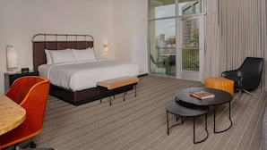 A hotel room with a bed, a desk, a chair, a small table, and a view of the outside. - Origin Baton Rouge, a Wyndham Hotel (Baton Rouge)